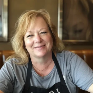 Smiling woman wearing a gray shirt and apron, standing in her home kitchen